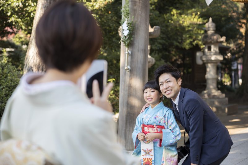 神社で七五三の写真をスマホで撮影するお母さん